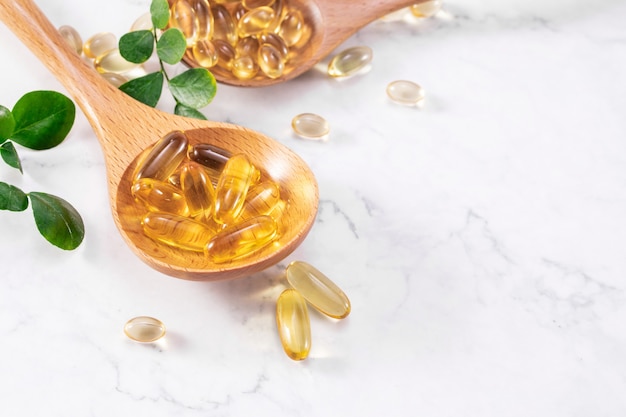 Selective focus shot of fish oil capsules on a wooden spoon with green leaves