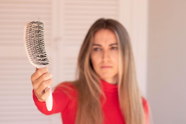 Selective focus of side view hair brush with a lot of fallen hair on it and young woman on red in the blurred background