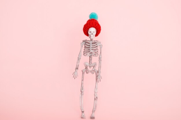 Selective focus skeleton wearing cute knitted hat on a pink background