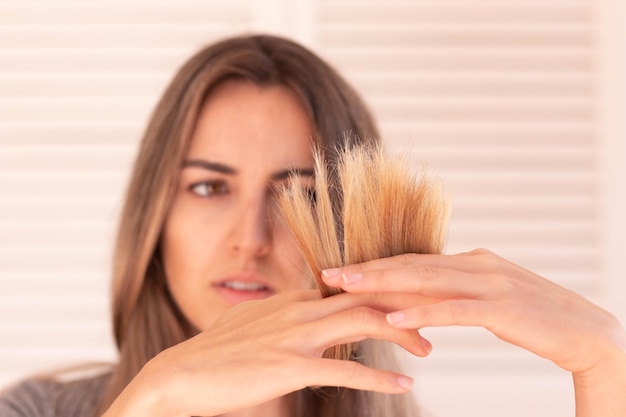 Selective focus of split ends in blond hair holded by blurred young woman in the background