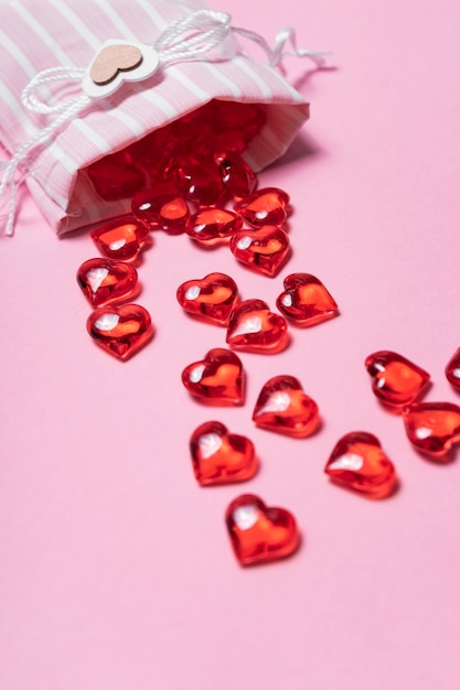 Selective focus. Valentine's day card. glass red hearts scattered from a beautiful cloth bag. the view from the top. pink background