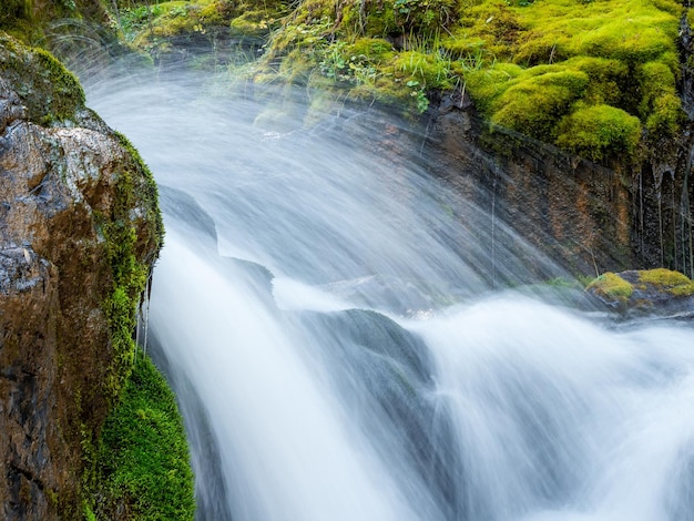 Selective focus. Waterfall close-up, water splashes, wildlife concept. Atmospheric minimal landscape with a long exposure of a large waterfall on a green rock.