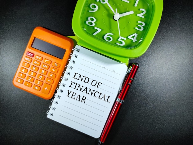 Selective focusWord END OF FINANCIAL YEAR on notebook with penclock and calculator on black backgroundBusiness concept