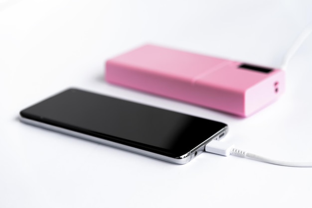 Selective soft focus photo of charging smart phone with pink color power bank on white background