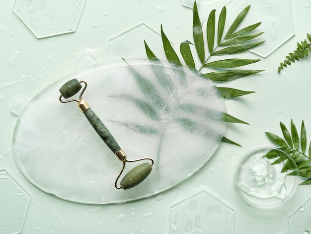 Self made moisturizer and green jade face roller on oval piece of ice with ice cubes