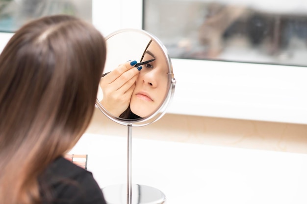 Self makeup Young woman looking in the mirror paints her eyebrows with a pencil