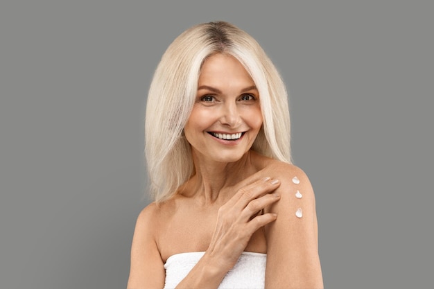 Self pampering concept beautiful mature lady applying body cream on shoulder