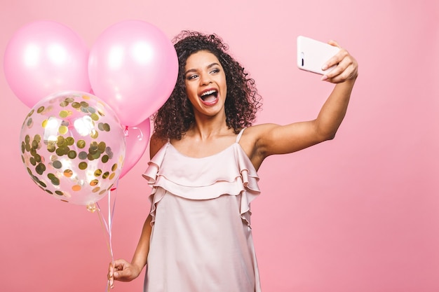 Self portrait of afro american positive girl in dress having balloons in hand shooting selfie