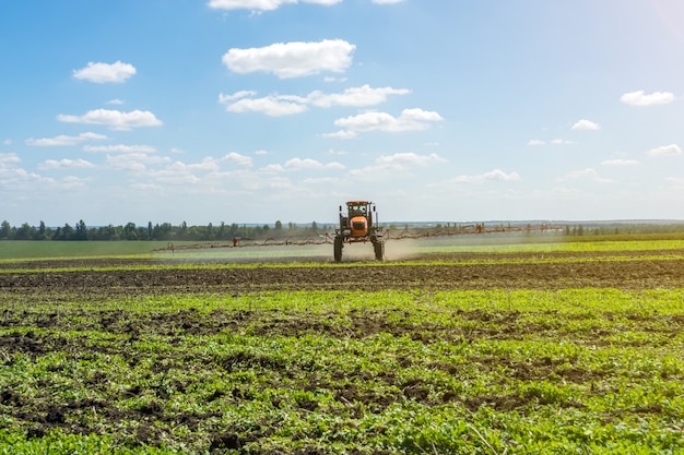 Self-propelled sprayer works on a field under a blue sky with clouds