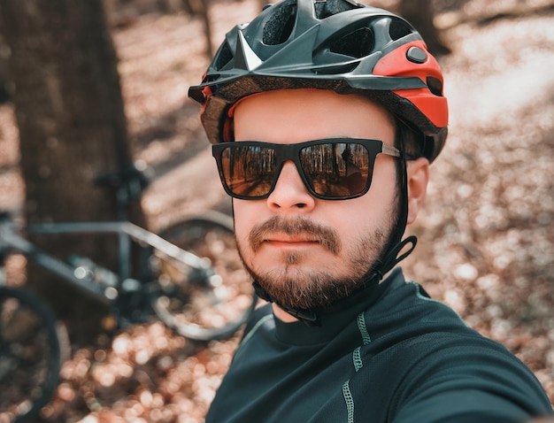 Selfie of a bearded man in cycling helmet wearing glasses A portrait of adventurer with his bicycle