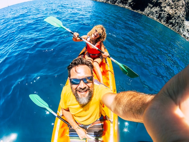 Selfie couple with top vertical point of view - happy active adult people enjoy kayak at the ocean - summer tourist in holiday vacation lifestyle - action camera and cheerful man and woman