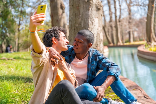 Selfie of a multiethnic gay male couple talking in the park by a river lgbt concept