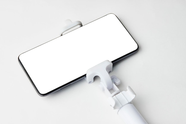 Selfie stick with smart phone on white background with copy space Monopod selfie stick and phone with blank white display closeup