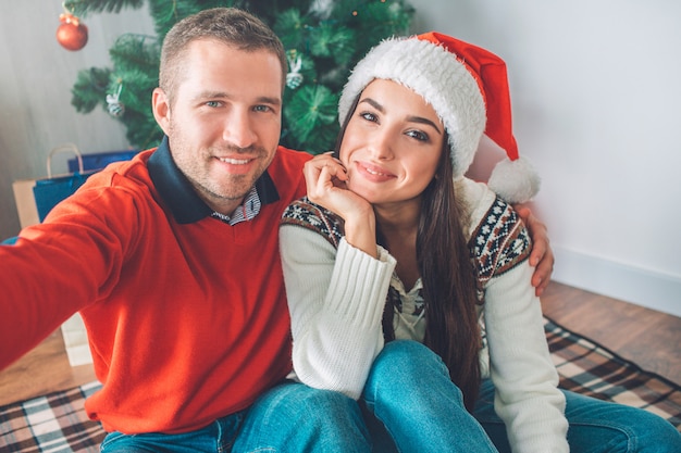 Selfie of two young people looking on camera and smile. He holds it with hand. 