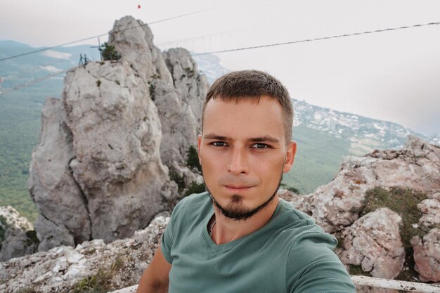 A selfie of a young male tourist climbing to the top of a cliff with a backpack Behind the cliff The concept of active life and hiking