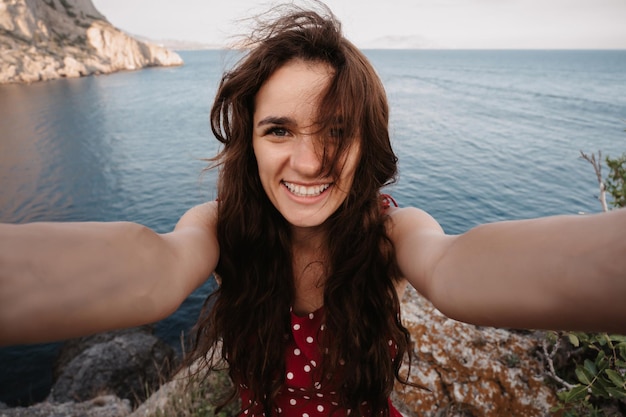 Selfieportrait of a young woman against the background of the sea at the cliff The girl smiles at the camera The concept of tourism recreation