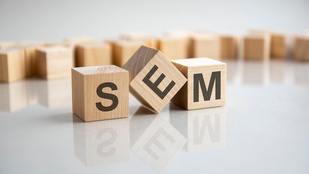 SEM - Search Engine Marketing acronym concept on cubes, gray background. Reflection on the mirrored surface of the table. Selective focus.