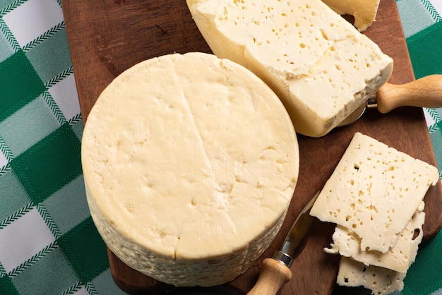 Semi-cured cheese from Brazil arranged on a rustic board on a green and white checkered tablecloth, selective focus.