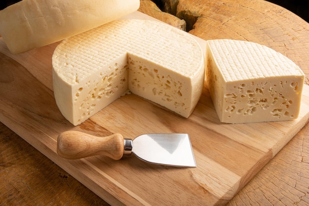 Semi-cured cheese from Brazil, beautiful Brazilian cheeses and cutting accessories arranged on light rustic wood, selective focus.