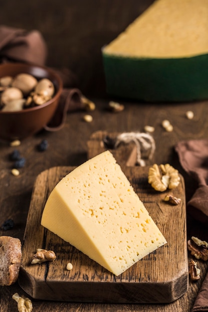 Semi-hard aged cheese with a rich taste with nuts on a wooden board. Dark wooden background. Side view close-up.