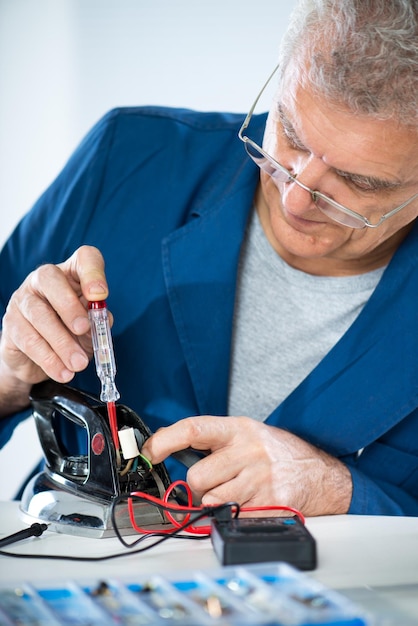 Senior adult Electrician using Electrical test pen for check mains voltage on old iron. Close Up.