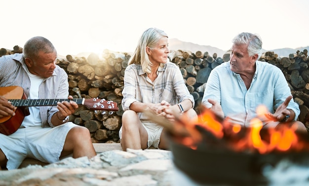 Senior adventure and fun wellness hiking group of friends relaxing or taking a break by the campfire after walking on outdoors mountain trip Elderly explorers resting on camping getaway trip