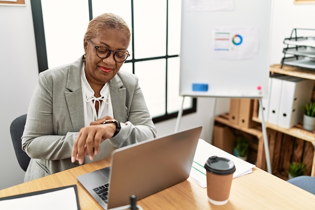 Senior african american woman business worker looking watch at office