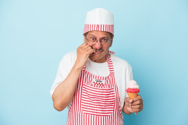 Senior american ice cream man holding an ice cream isolated on blue background biting fingernails, nervous and very anxious.