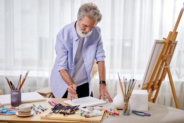 Senior artist draws a sketch on paper, and then on canvas, stands drawing, in light room