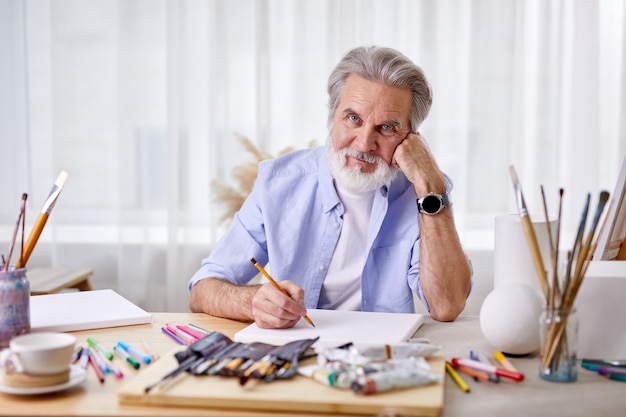 Senior artist sit thinking, . mature man leaned on hand, engaged in drawings, creating masterpiece