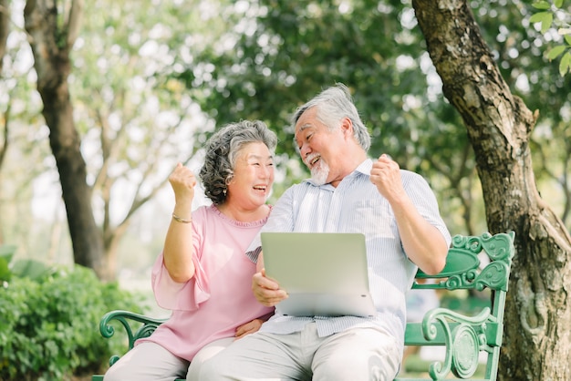 Senior Asian couple laughing with laptop in park