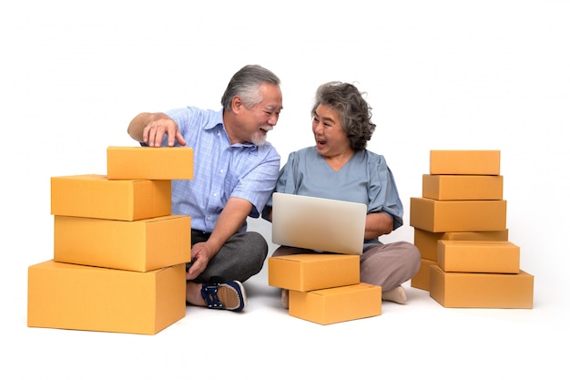 Senior asian couple startup small business freelance holding parcel box and computer laptop and sitting on floor, Online marketing packing box delivery concept