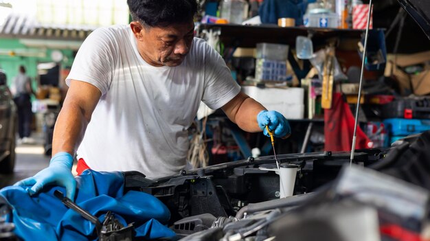 Senior asian male auto mechanic worker checking oil level in car engine at Car Service station Car maintenance and auto service garage concept