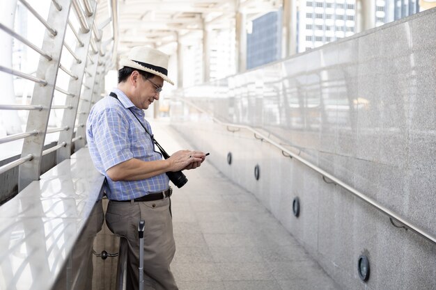 Senior Asian man play mobile phones in airports to prepare to travel abroad.