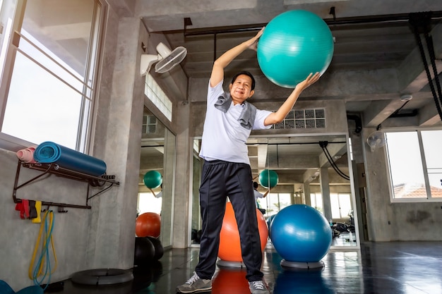 Senior Asian man in sportswear training abdominal muscles with ball gym at fitness.