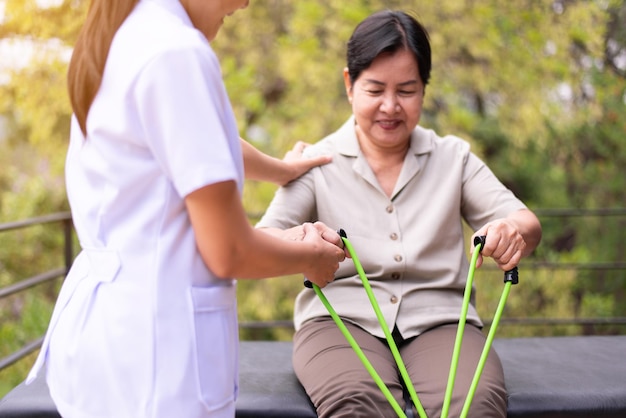 Senior asian woman doing exercises and stretching for treatment with a rubber resistance bands with nurse at homePhysical therapy conceptxA