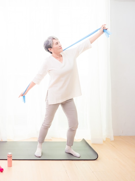 Senior asian woman doing exercises with resistance band at home.