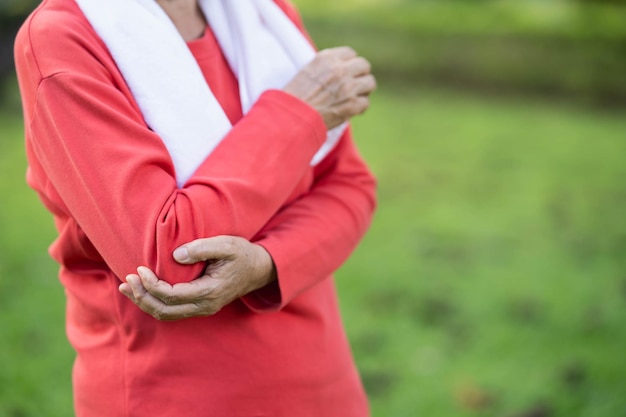 Senior asian woman hold arm or elbow pain after running in park Old asian woman resting at the park garden and holding painful elbow Sport and health concept