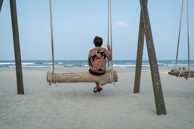 Senior Asian woman relaxing on a wood plank swing on the beach