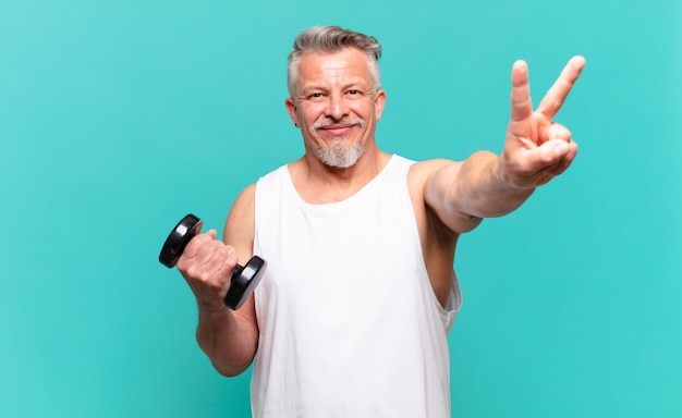 Senior athlete man smiling and looking happy, carefree and positive, gesturing victory or peace with one hand