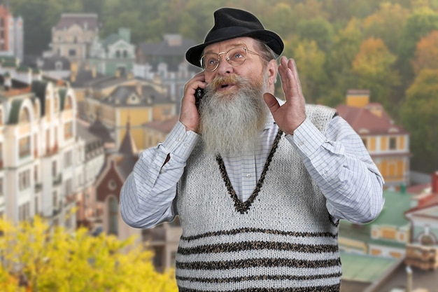 Photo senior bearded man in hat talking on the mobile phone.