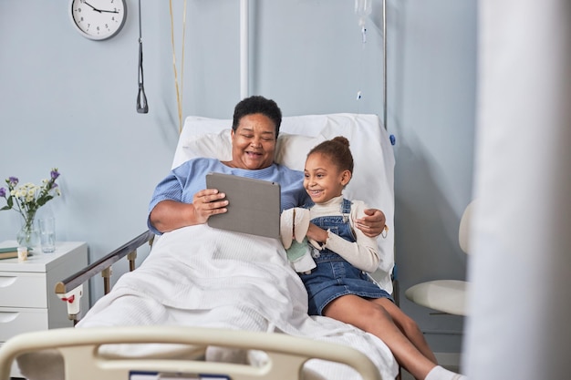 Senior black woman with little girl using digital tablet in hospital room