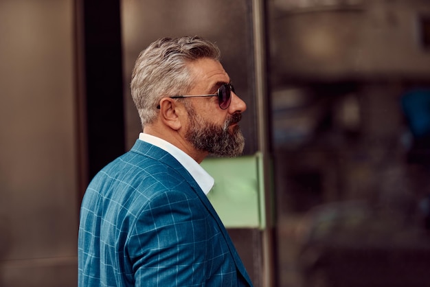 Senior businessman in a blue suit posing on a city street.