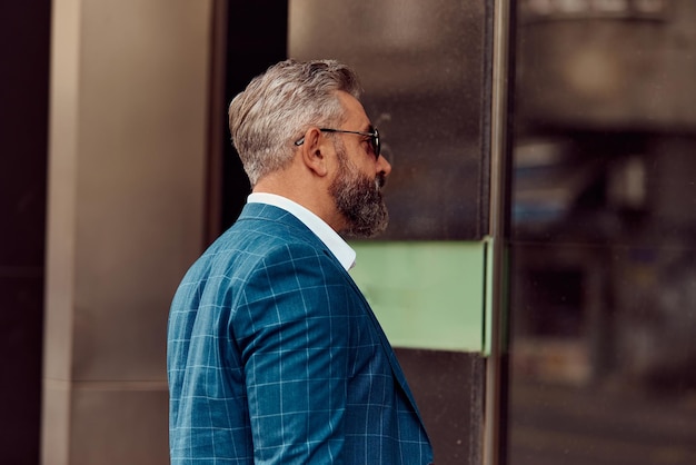 Senior businessman in a blue suit posing on a city street.