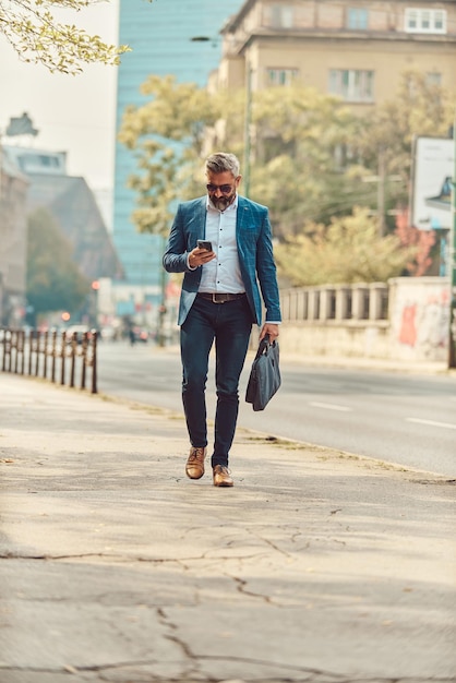 A senior businessman in a blue suit in an urban environment using a smartphone.