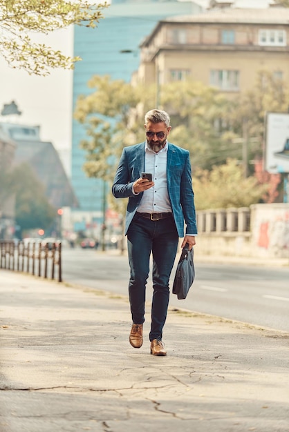 A senior businessman in a blue suit in an urban environment using a smartphone.