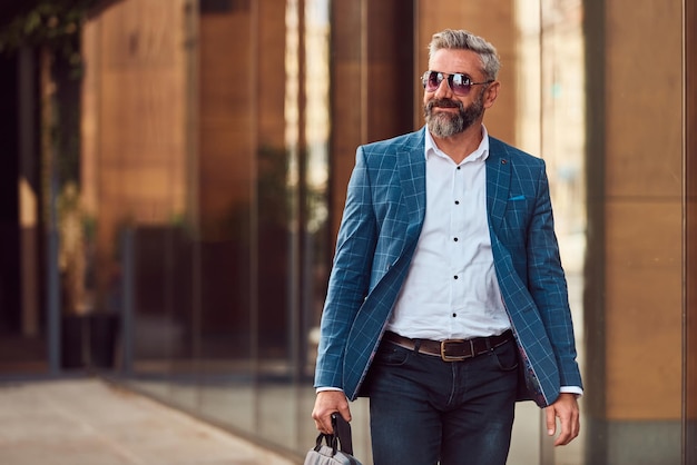 A senior businessman in a blue suit with a briefcase walking through the city.