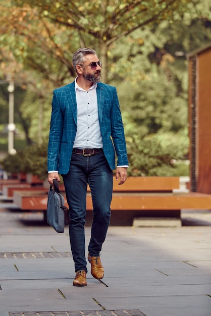 A senior businessman in a blue suit with a briefcase walking through the city.