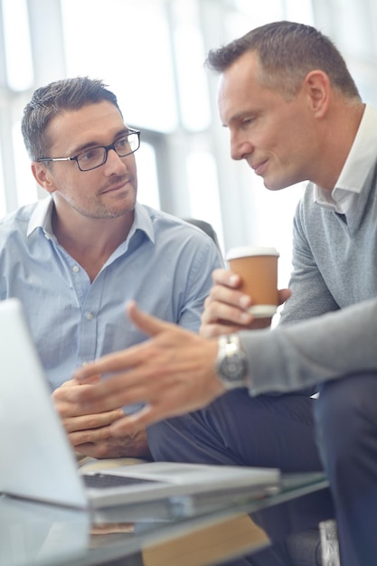 Senior businessman laptop and colleague in discussion for deal proposal or idea at office Business people talking strategy or planning market strategy or advertising in conversation at workplace