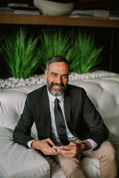 Senior businessman using mobile phone and sitting on the sofa in the office